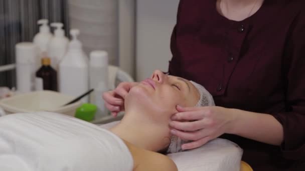 Donna cosmetologa professionista che fa il massaggio facciale a cliente di salone di bellezza . — Video Stock