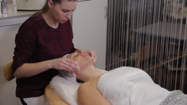 व्यावसायिक सौंदर्यशास्त्रज्ञ प्रक्रिया करण्यापूर्वी रुग्णाला चेहरा धुतात . — स्टॉक व्हिडिओ