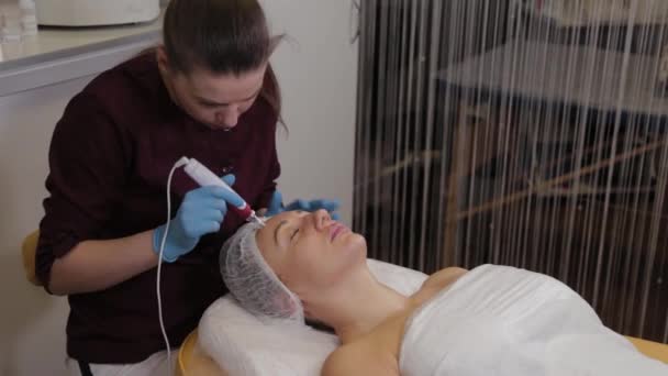 Professional beautician woman performs micronidling facial skin. — Stockvideo