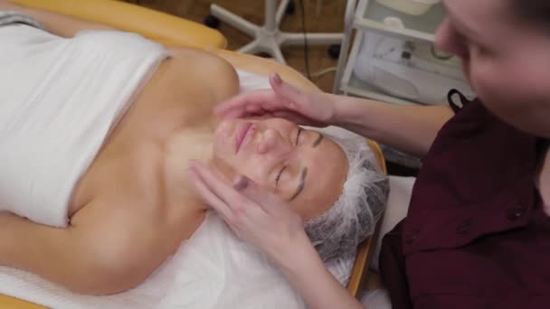 Donna cosmetologa professionista che fa il massaggio facciale a cliente di salone di bellezza . — Video Stock