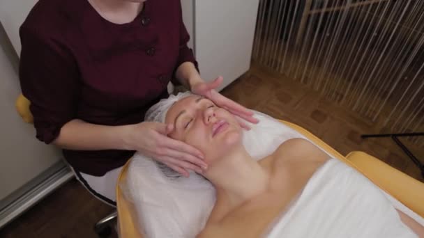 Cosmetologist profissional mulher fazendo massagem facial ao cliente de salão de beleza . — Vídeo de Stock