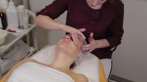 Cosmetologist profissional mulher fazendo massagem facial ao cliente de salão de beleza . — Vídeo de Stock