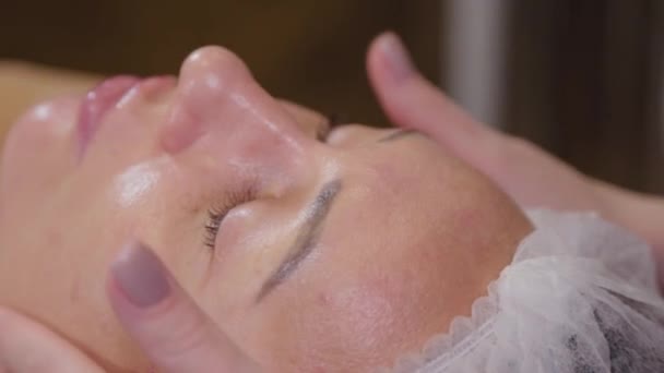 Професійний косметолог жінка робить масаж обличчя клієнту салону краси . — стокове відео