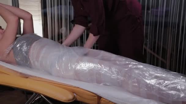 Professional beautician woman performs body wrap procedure in a beauty salon. — Stockvideo