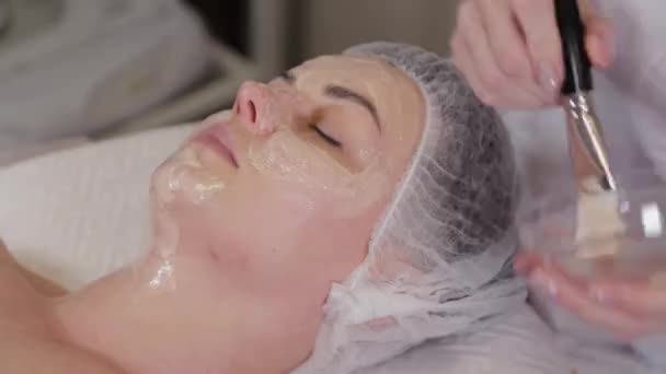 Mujer cosmetóloga profesional pone una máscara en la cara del paciente . — Vídeos de Stock
