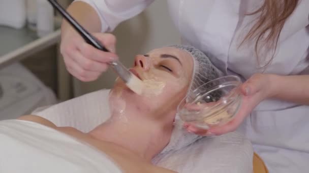 Donna cosmetologa professionista mette una maschera sul viso del paziente . — Video Stock