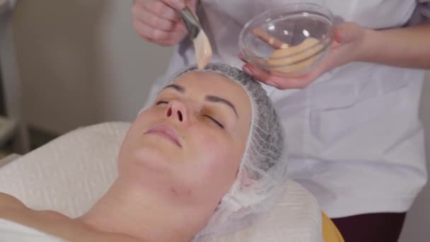 Mujer cosmetóloga profesional pone una máscara en la cara del paciente . — Vídeos de Stock
