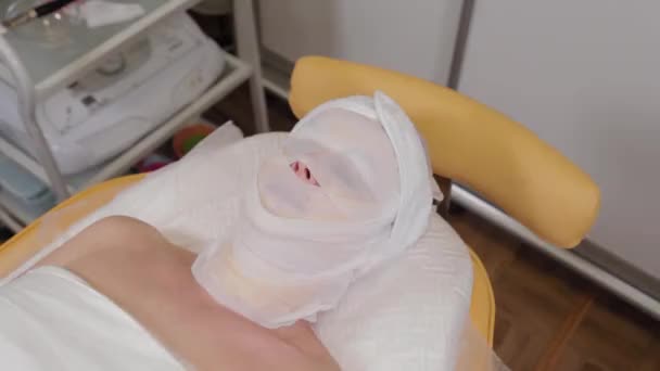 Mulher paciente encontra-se com ligaduras em seu rosto em um salão de beleza . — Vídeo de Stock