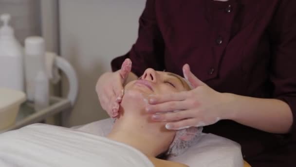 Een professionele schoonheidsspecialiste wast de patiënten gezicht met vloeibare zeep en tegelijkertijd massages. — Stockvideo