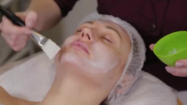 Cosmétologue professionnelle femme met un masque sur le visage du patient . — Video