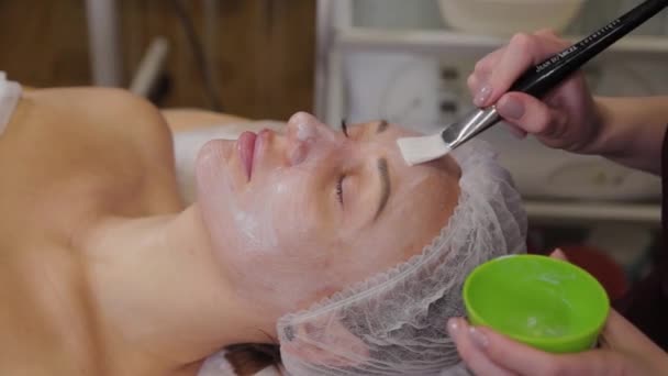 Donna cosmetologa professionista mette una maschera sul viso del paziente . — Video Stock