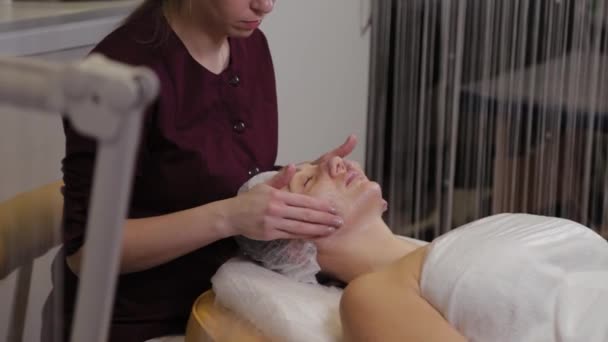 Cosmetóloga profesional haciendo masaje facial al cliente de salón de belleza . — Vídeo de stock