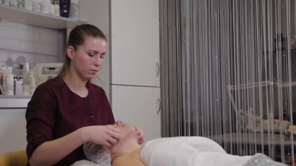 Cosmétologue professionnelle femme faisant massage facial au client du salon de beauté . — Video