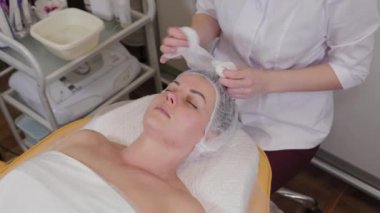 Professional beautician washes face to patient before procedure.