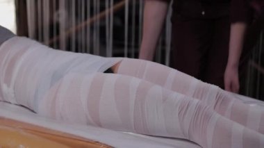 Professional beautician woman performs body wrap procedure in a beauty salon.