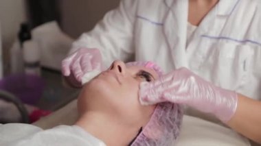 Profesyonel güzellik uzmanı pamuk pedlerle müşteriyle yüz yüze yıkanır.