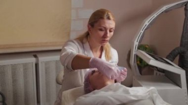 Profesyonel güzellik uzmanı bir fırçayla müşterinin yüzüne maske takıyor..