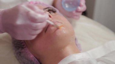 Profesyonel güzellik uzmanı bir fırçayla müşterinin yüzüne maske takıyor..