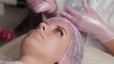 Profesyonel güzellik uzmanı bir fırçayla müşterinin yüzüne maske takıyor..