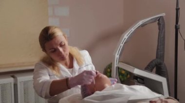 Profesyonel güzellik uzmanı bir fırçayla müşterinin yüzüne maske takıyor..