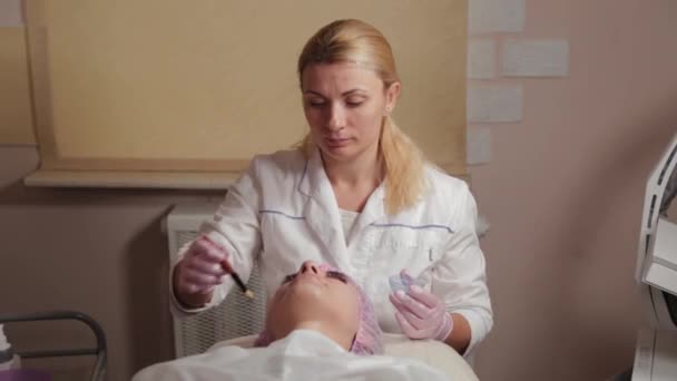 Professionell kosmetolog som applicerar en mask på klientens ansikte med en borste. — Stockvideo