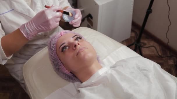 Esthéticienne professionnelle appliquant un masque sur le visage du client avec une brosse . — Video