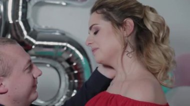 Beautiful man and woman cuddling near birthday balloons.