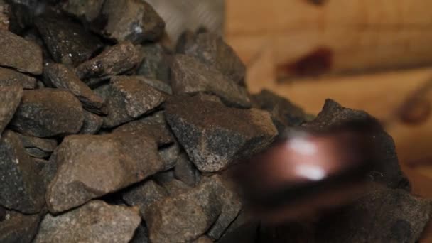 Un homme verse de l'eau sur des pierres chaudes dans un sauna . — Video