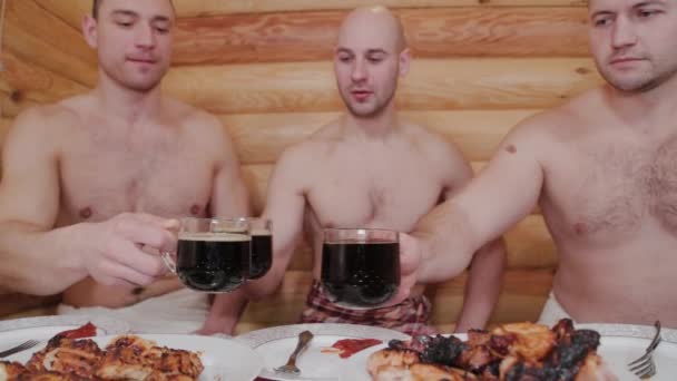 Young sports men in a sauna with beer and meat on the table. — 비디오