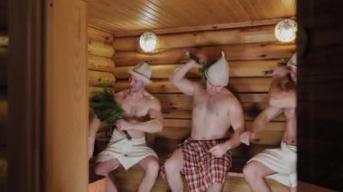 Süpürgelerle saunada süzülen atletik adamlar..
