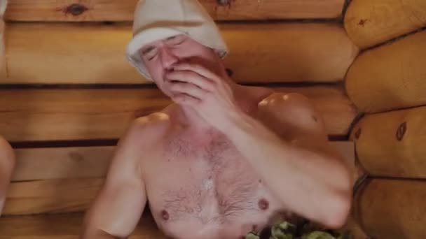 Hombres atléticos se elevan en una sauna con escobas . — Vídeo de stock