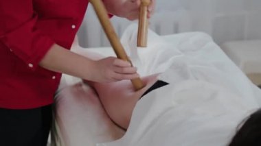 Masaj salonundaki müşteriye bambu çubuklarıyla masaj yapan kadın masaj terapisti..