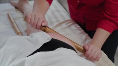Masaj salonundaki müşteriye bambu çubuklarıyla masaj yapan kadın masaj terapisti..