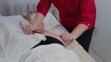 Masaj salonundaki müşteriye bambu çubuklarıyla masaj yapan kadın masaj terapisti..