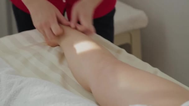 Weibliche Massagetherapeutin massiert Klienten Beine. — Stockvideo