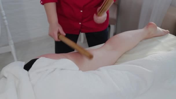Masajista femenina haciendo masaje con varillas de bambú al cliente en salón de masajes . — Vídeos de Stock