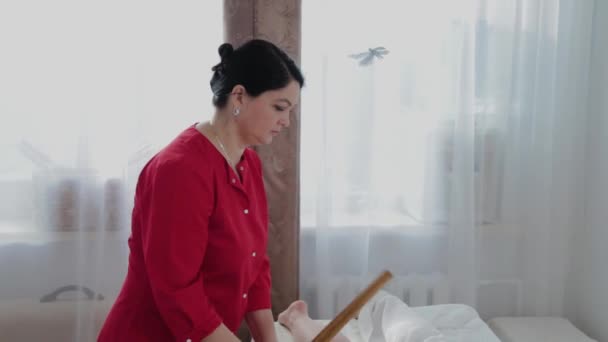 Γυναίκα θεραπεύτρια μασάζ κάνει μασάζ με μπαμπού μπαστούνια στον πελάτη στο σαλόνι μασάζ. — Αρχείο Βίντεο