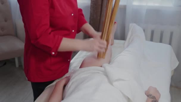 Female massage therapist doing massage with bamboo sticks to client in massage parlor. — 비디오