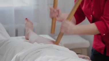Masaj salonundaki müşteriye bambu çubuklarıyla masaj yapan kadın masaj terapisti..
