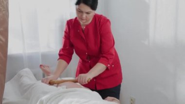 Masaj salonundaki müşteriye bambu çubuklarıyla masaj yapan kadın masaj terapisti..