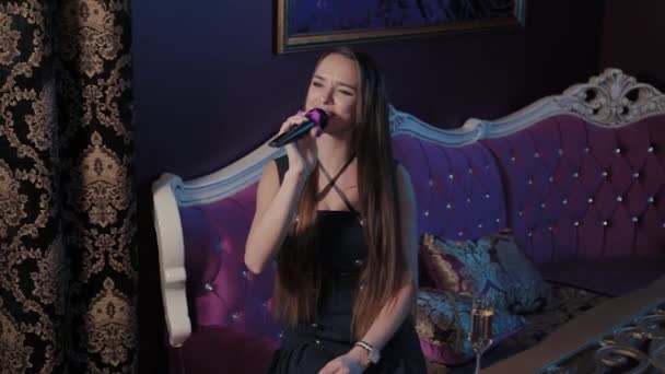 小女孩在卡拉OK俱乐部的沙发上对着麦克风唱歌. — 图库视频影像