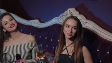 Güzel genç kızlar bir kanepede karaoke kulübünde şarkı söylüyorlar..