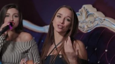 Güzel genç kızlar bir kanepede karaoke kulübünde şarkı söylüyorlar..