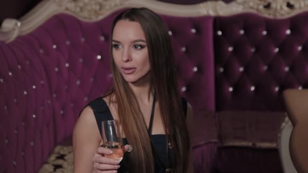 Beautiful young woman with a glass of champagne in a restaurant interior. — Stock Video