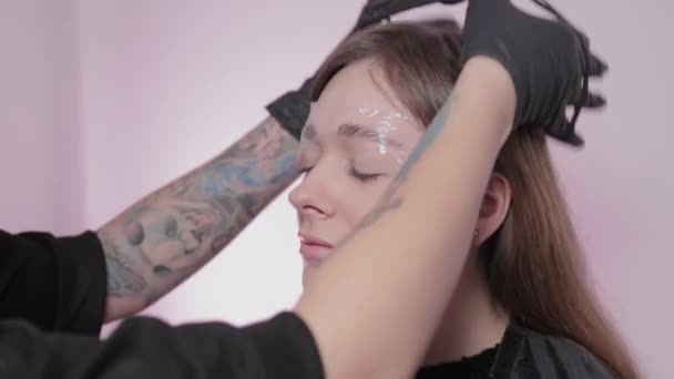 Professional woman eyebrow master puts film on eyebrows in a beauty salon. — Stock Video