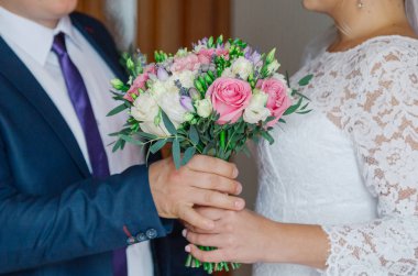 Young and happy bride and groom holding a wedding bouquet in their hands.