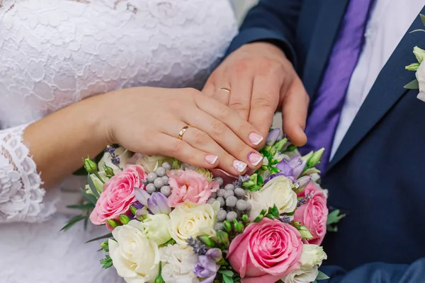 Belle mani con fedi nuziali degli sposi su un mazzo . — Foto Stock