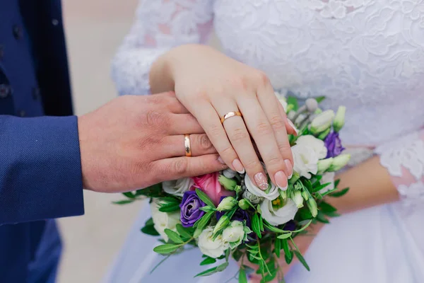 Prachtige handen met trouwringen van de pasgetrouwden op een boeket. — Stockfoto