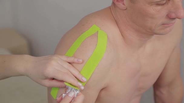 De dokter lijmt een speciale behandeling tape aan een man. — Stockvideo