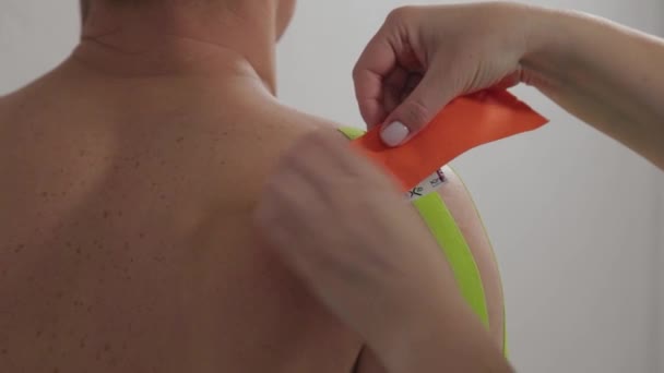 De dokter lijmt een speciale behandeling tape aan een man. — Stockvideo